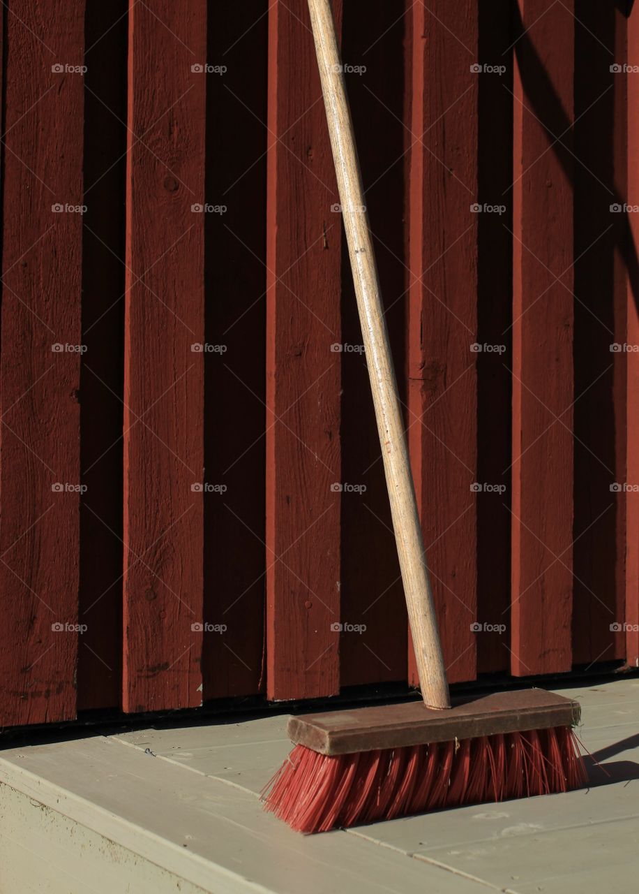 A red piassava broom against the red wall. 