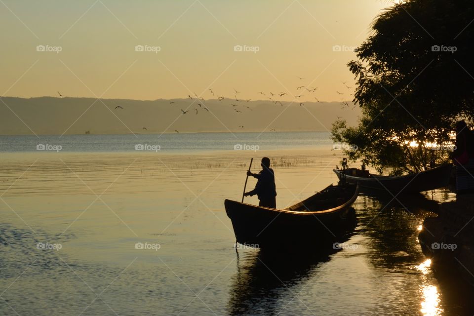 A man rowing a boat towards lake mooring at sunrise