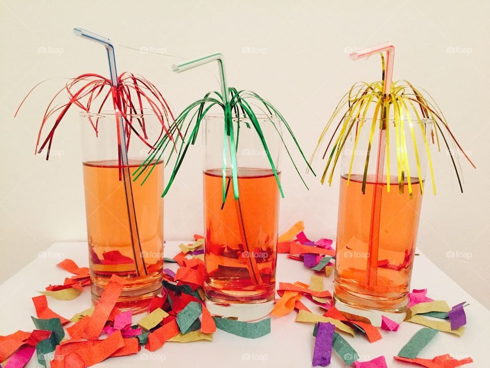 Three cocktails with decorated straws on a table with confetti