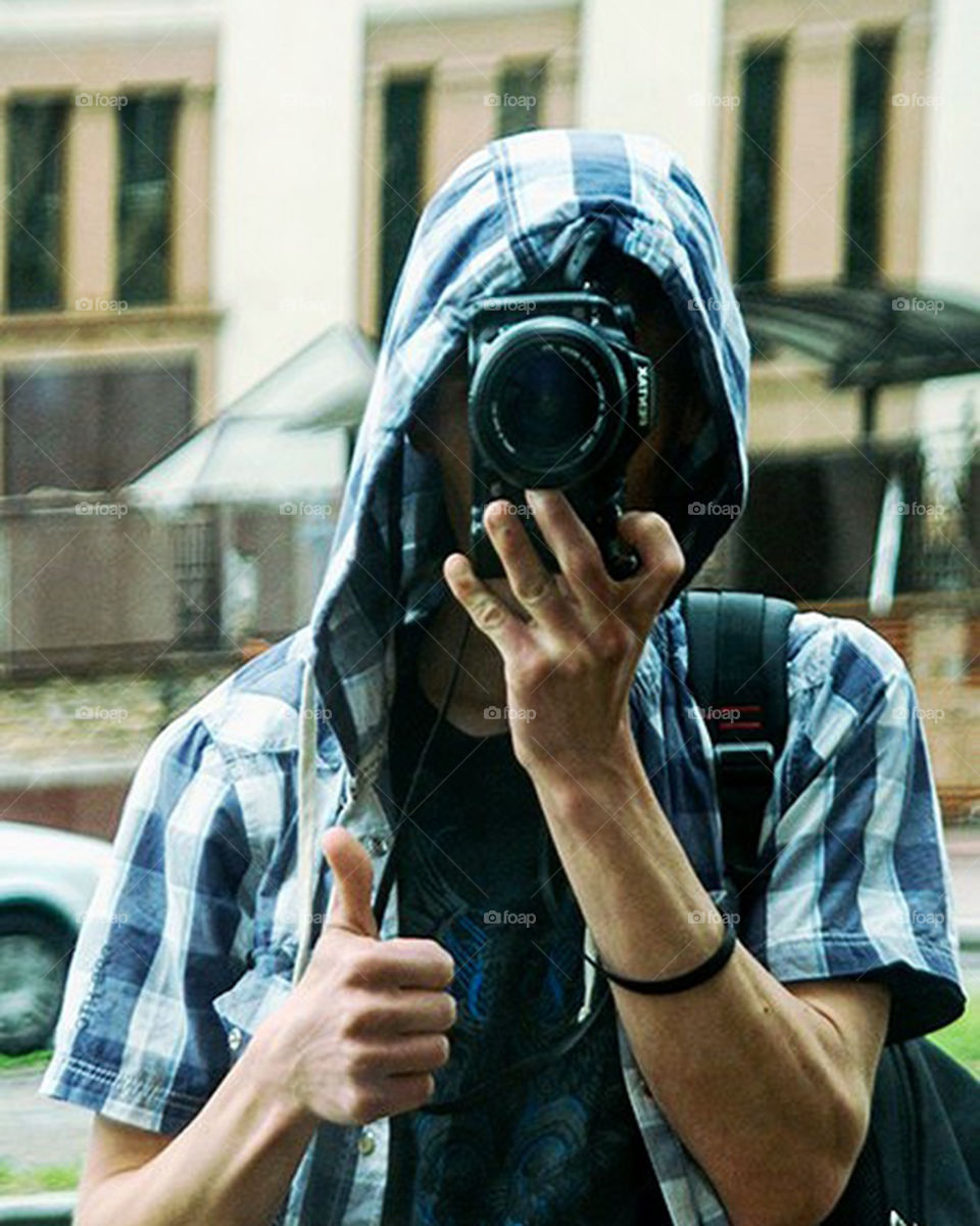 Selfie photographer in a blue shirt with a hood on a reflex camera in a reflection of shop windows