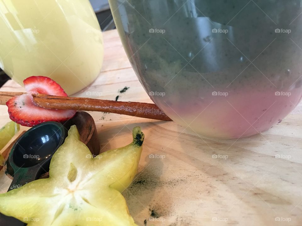 Low angle view of green and white fresh fruit smoothies in layers of color  garnished with  cinnamon stick with heart shaped strawberry, star fruit and honey almond smoothie in background with green protein powder