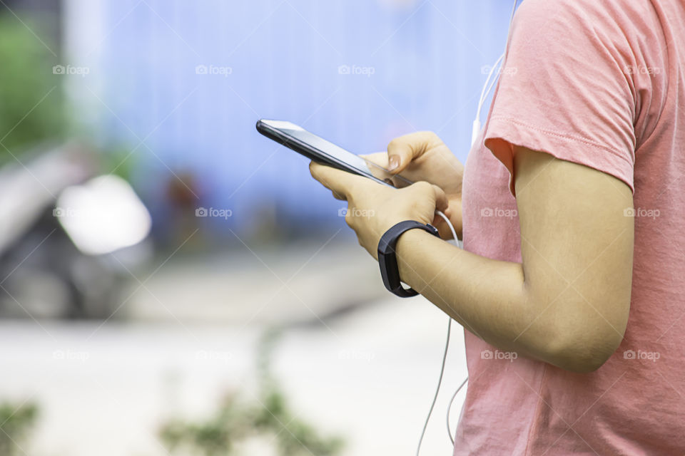 Hand of a woman wearing a watch and holding the phone plugged in headphones.