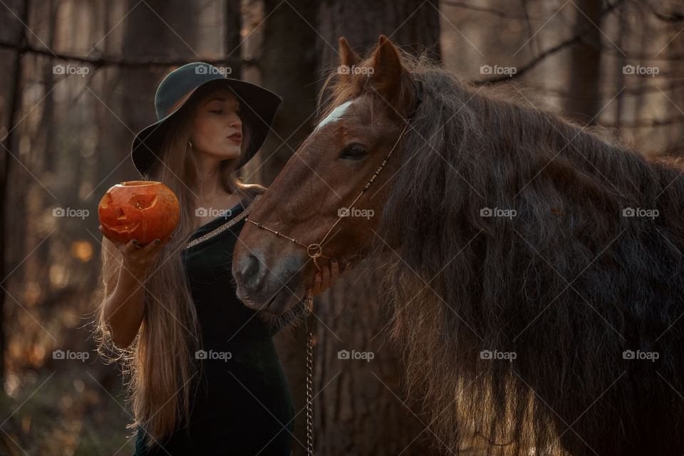Woman in witch wear with horse in autumn park 