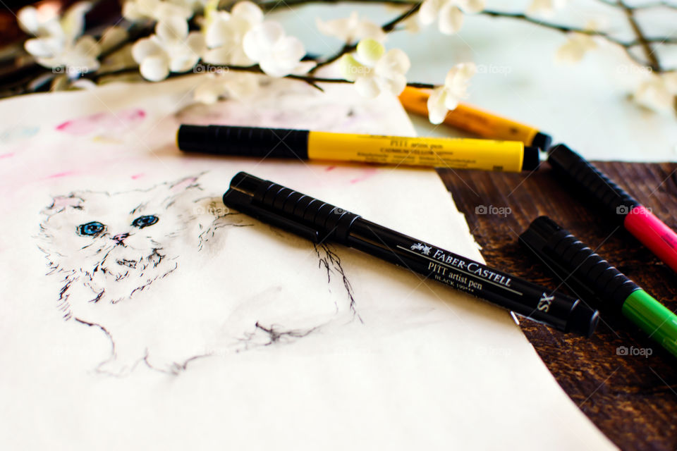 Artist workshop spring table with flowers and Faber-Castell PITT artists pens on sketchbook with sketch of white kitten made using smudging, water (watercolor) and sketch techniques of the PITT pens tranquility and creativity conceptual photography