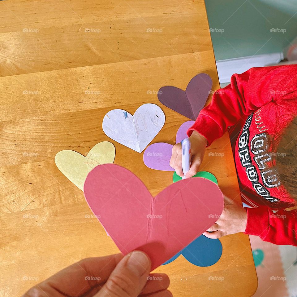 Toddler making Valentine’s Day hearts, child doing crafts indoors, craft time indoors in the winter time, winter time children’s crafts, making valentines, toddler playing with paper hearts, making Valentines Day decorations with a toddler