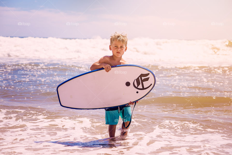 Cute boy holding surfboard on sea