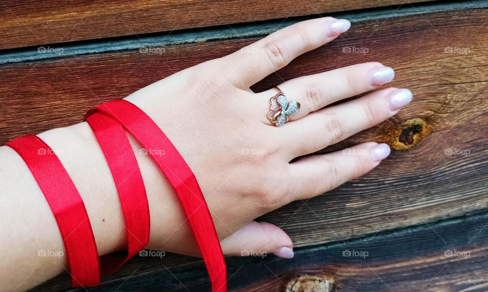 female hand with a red ribbon and a ring on the background of the wall of a wooden house.