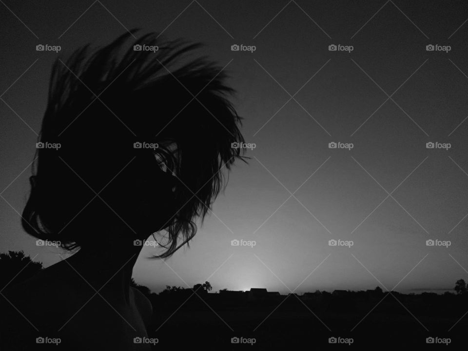 Silhouette of woman doing hair flip on sunset background in black and white