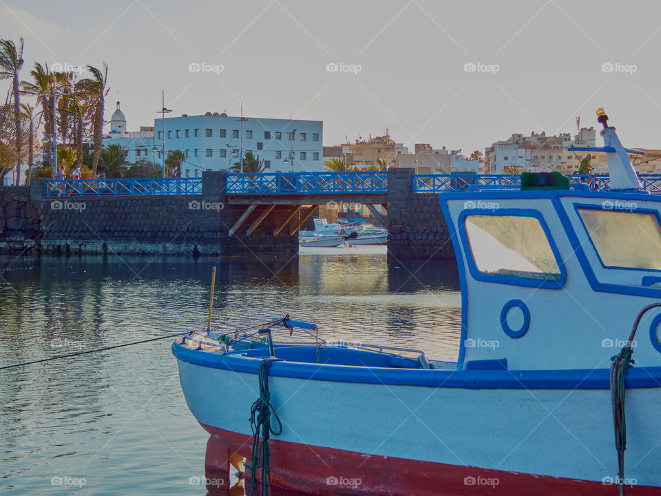 Paisaje pesquero con barco en primer plano y puente de piedra y madera de fondo con luz de el atardecer