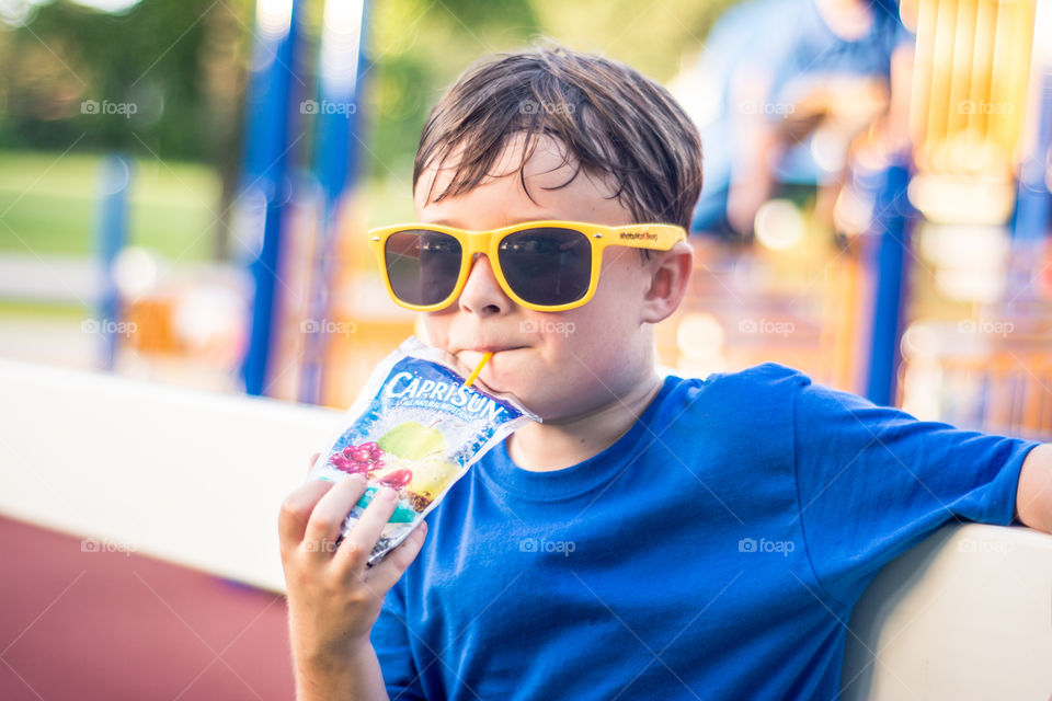 Young Boy Wearing Yellow Sunglasses Drinking Capri Sun at the Playground 2