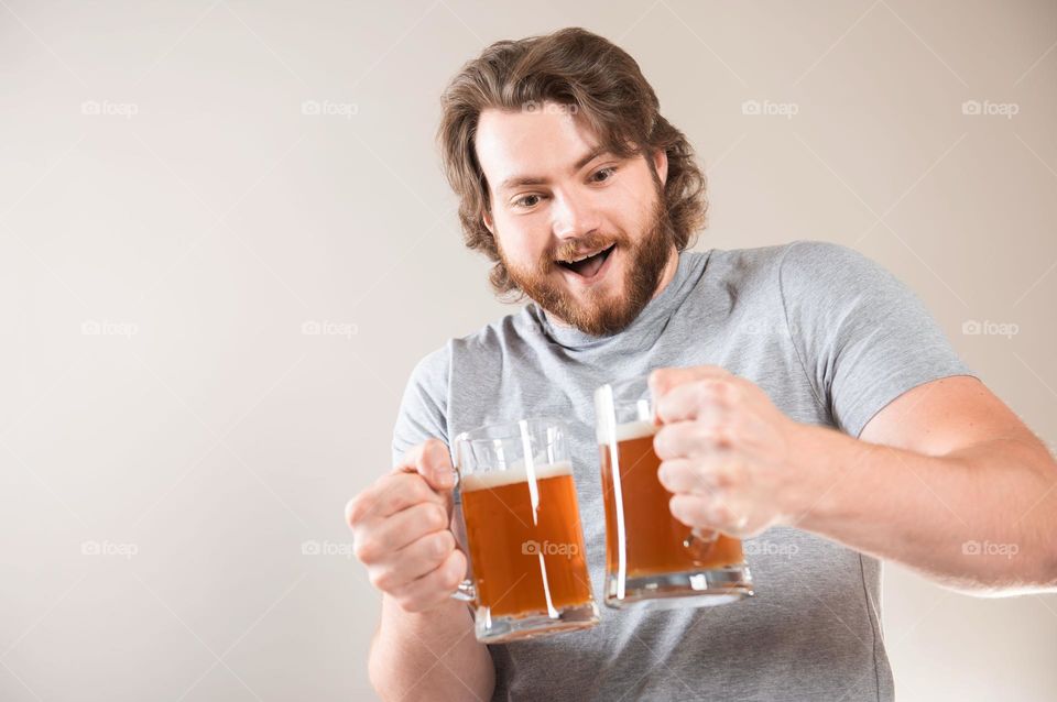 Excited young bearded man with two mugs of beer