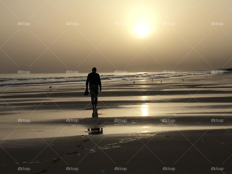Lonely man walking on a beach at sunset