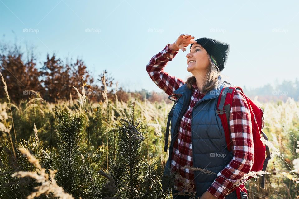 Young woman enjoying the view of mountains. Woman standing on trail and looking at view. Woman with backpack hiking through tall grass along path in mountains. Spending summer vacation close to nature