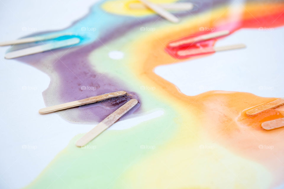 Close-up of melted popsicles with the popsicle sticks left behind and colors mixed together