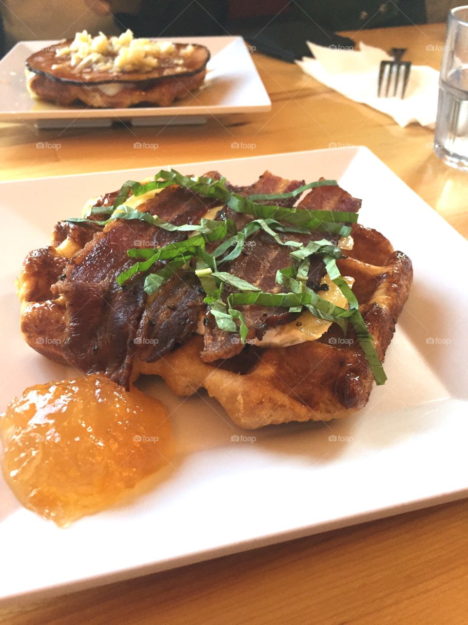 Waffle with bacon, cheese and basil with peach jam on the side on a square plate