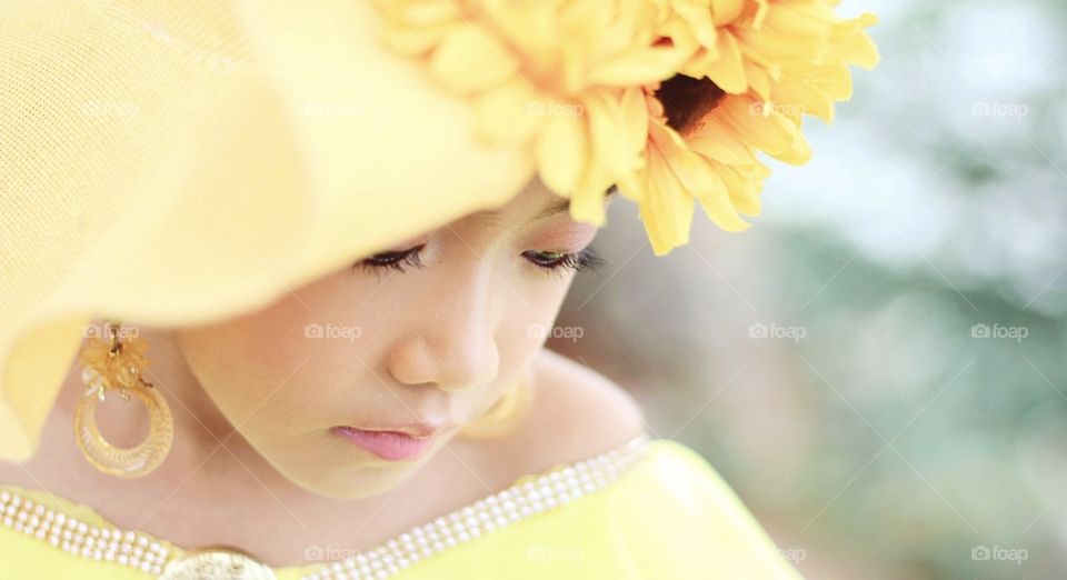 A beautiful baby girl wearing sunflower hut and yellow dress she looks more stunning in it with a simple shot and angle looks.