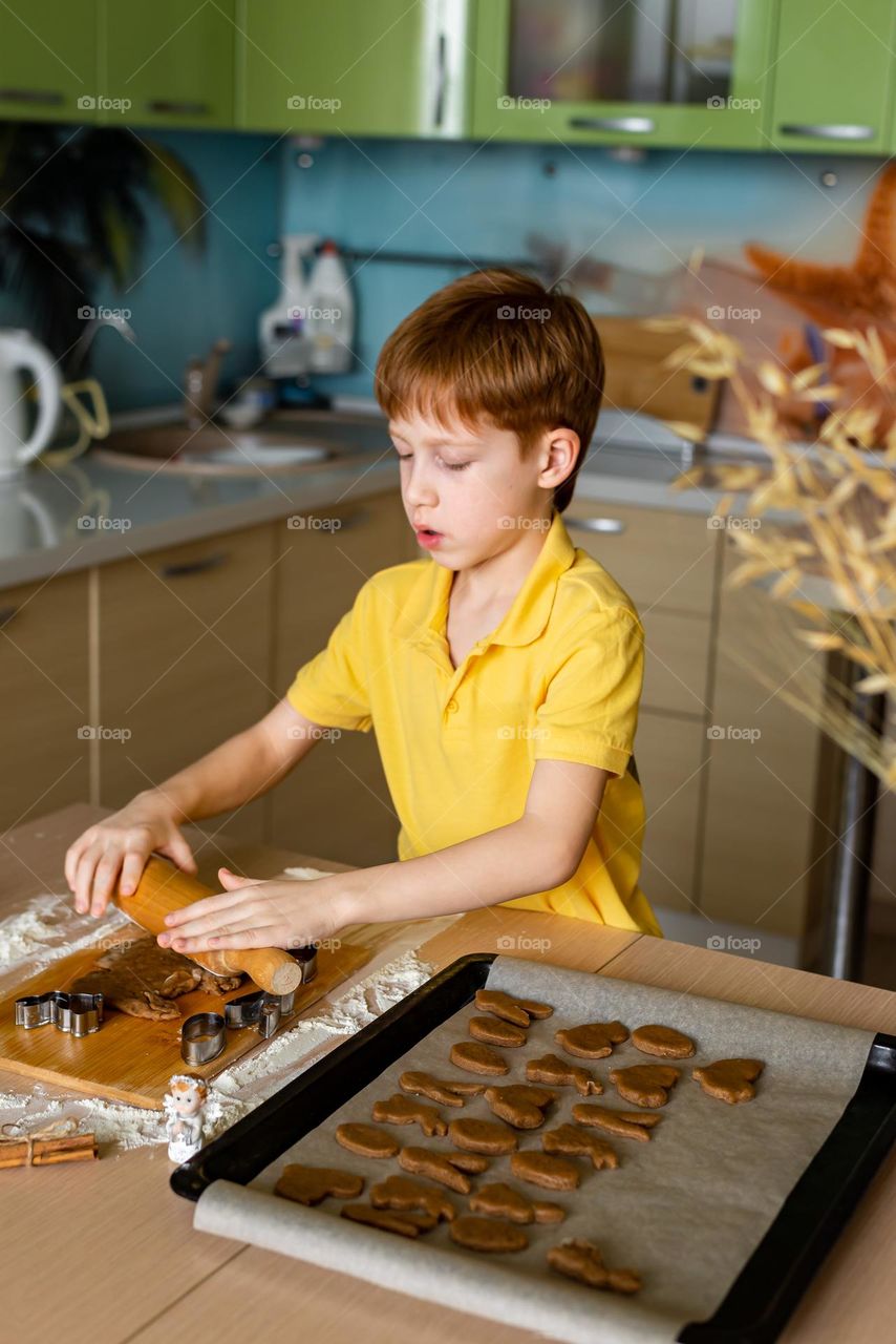 Cooking homemade cookies. The red-haired boy rolls out the dough for baking. Do it yourself, craft product