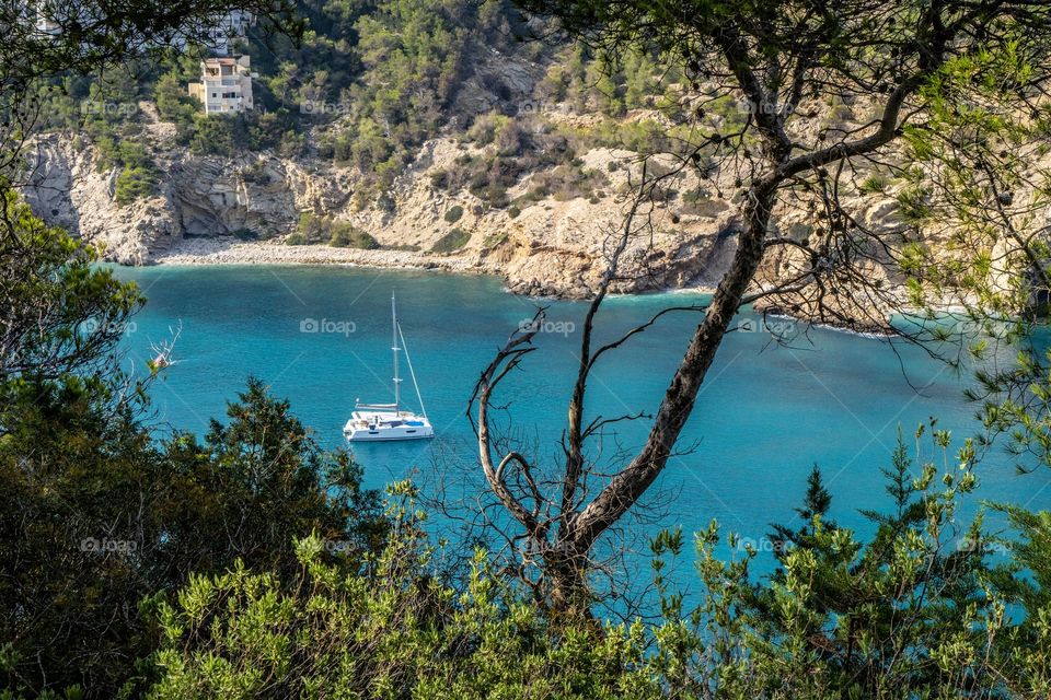 A yacht sits in the beautiful turquoise sea of Cala Llonga, Ibiza. Cala llonga is one of the many beautiful resorts around the island. 