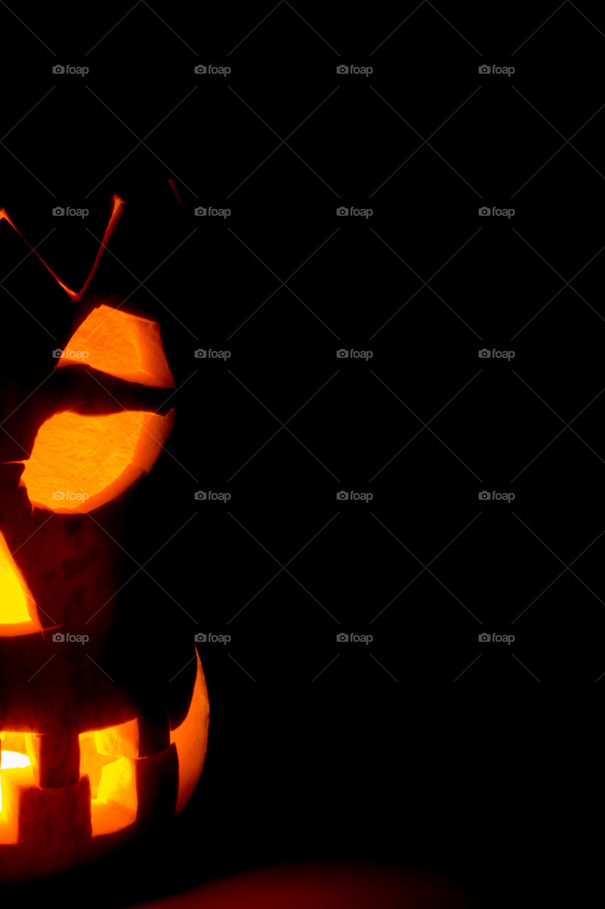 Half of an evil pumpkin close-up glowing in a dark room.
