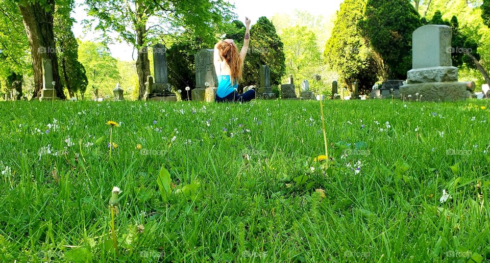 Red headed woman doing yoga facing away in a Cemetery surrounded by Headstones