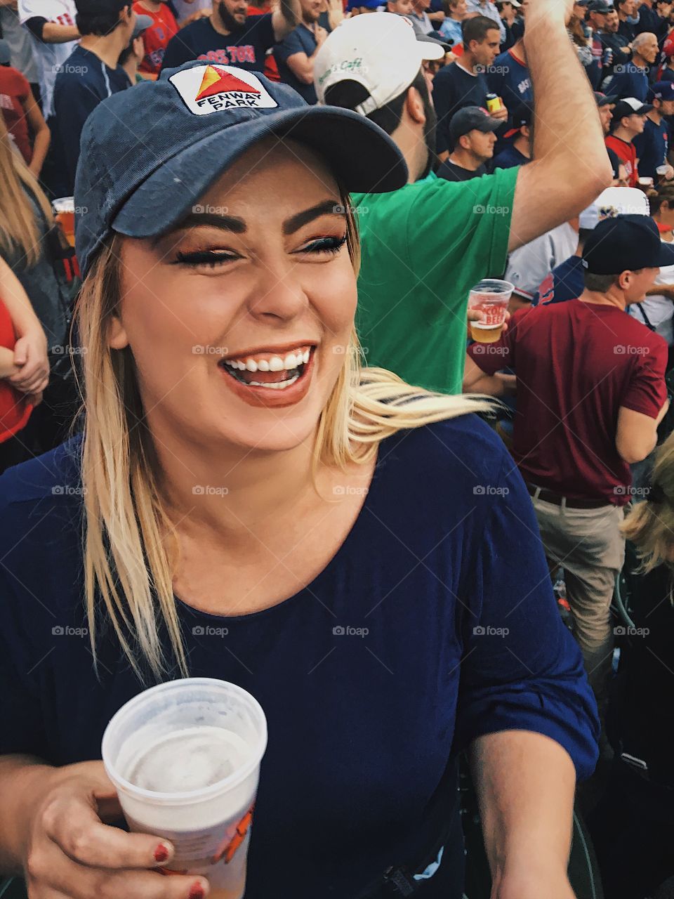 Blonde Girl laughing and having fun drinking beer at Boston Red Sox baseball game 