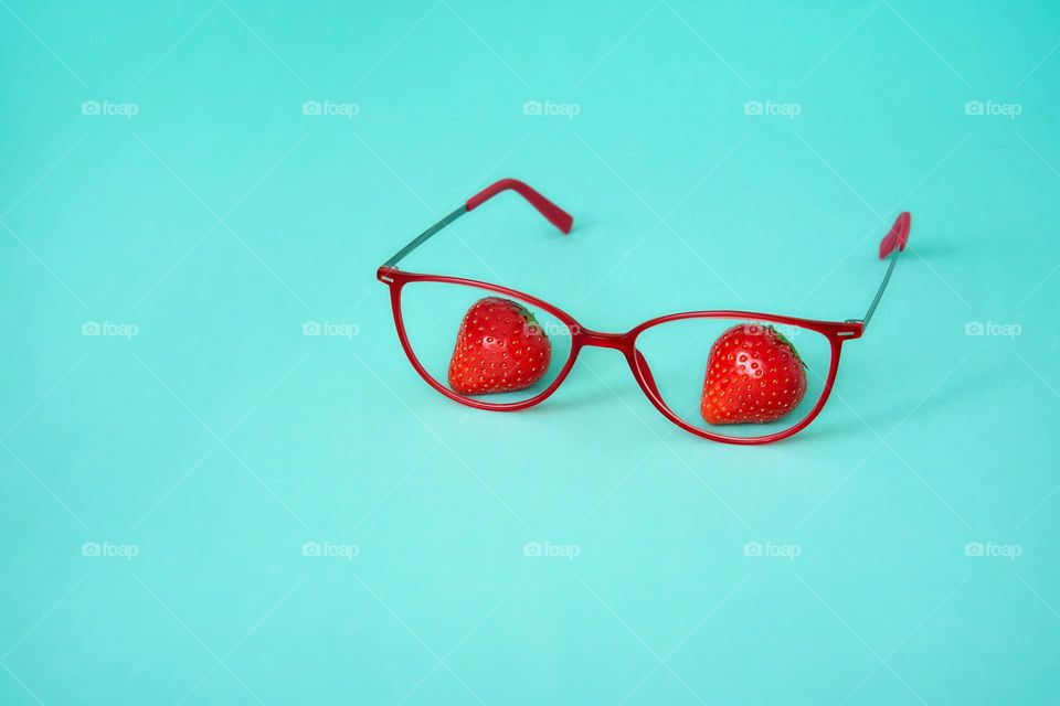 Red frame glasses with strawberries on a turquoise background 