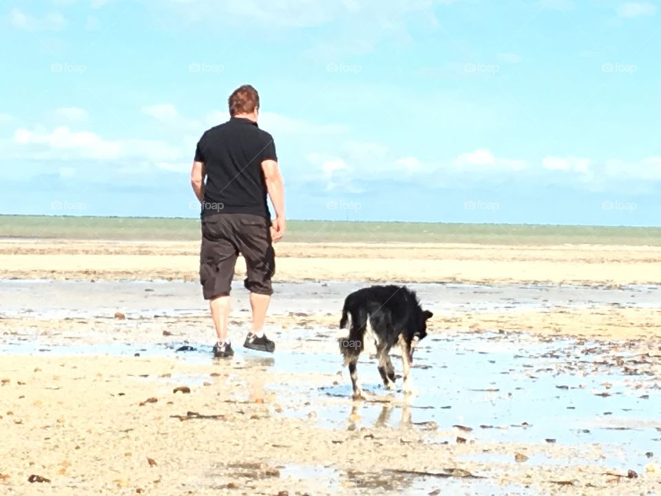 Man walking dog on secluded beach at low tide 