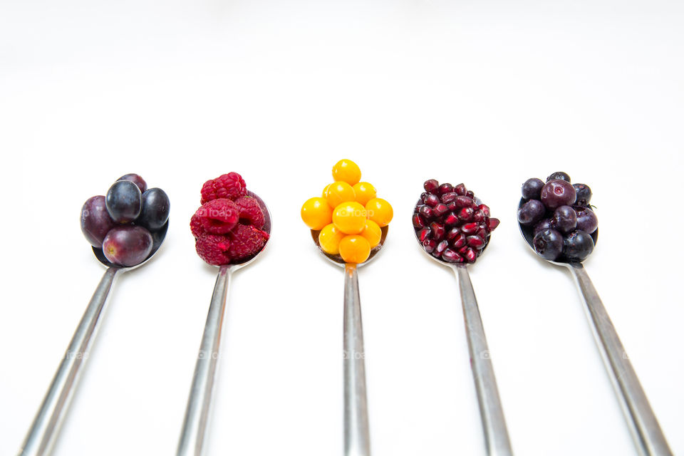 Fruits stacked on spoons. Fresh sure fruit. Variety of superfoods for a healthy diet including grapes raspberries gooseberries pomegranates and blueberries. Close up on a white background.