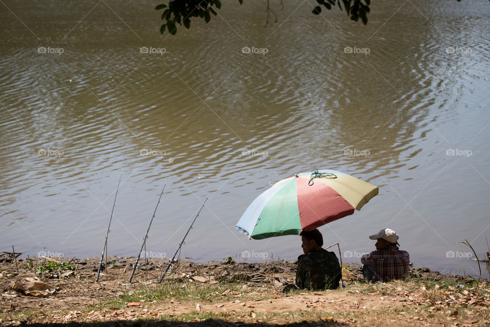 Man fishing on the river with umbrella 