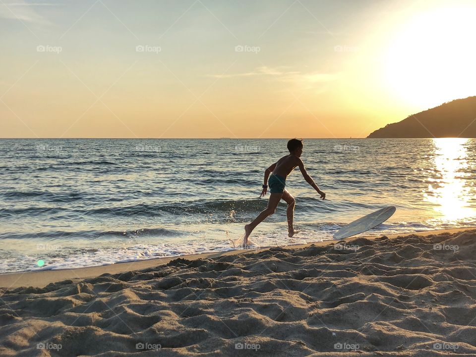 Boy playing with surfboard on the seashore at the sunset