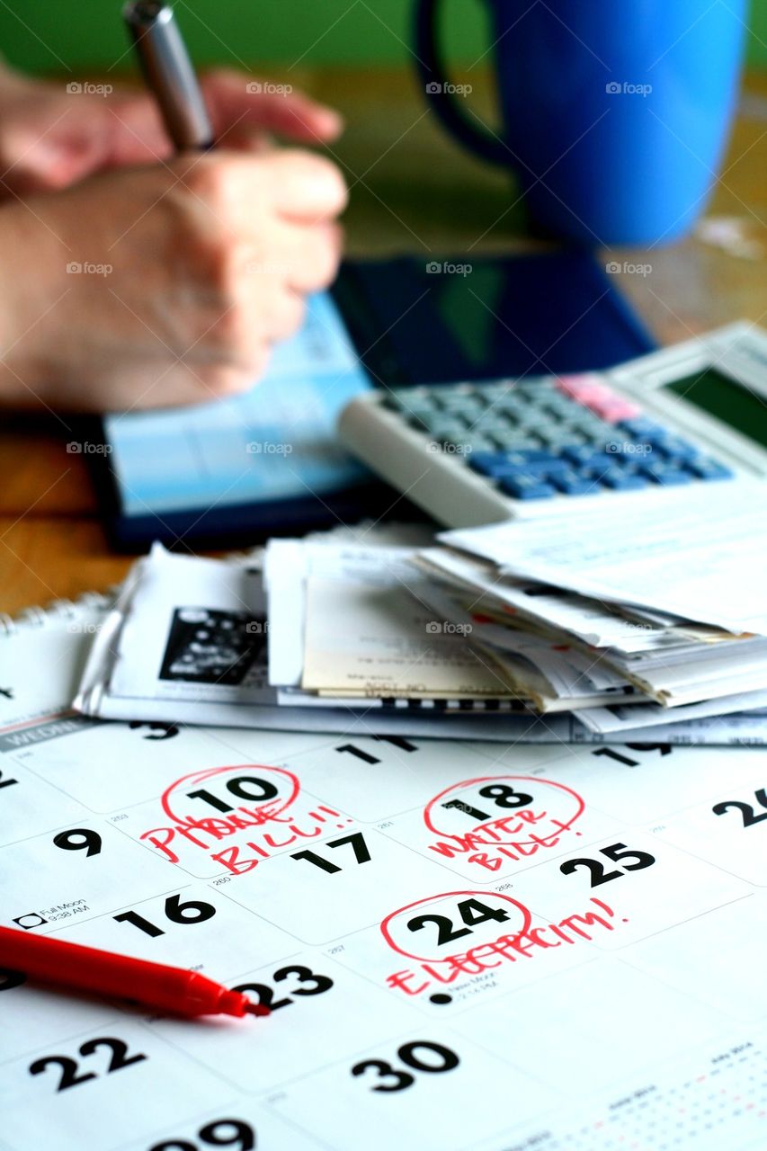 calendar, calculator, bills and a person writing on a check book