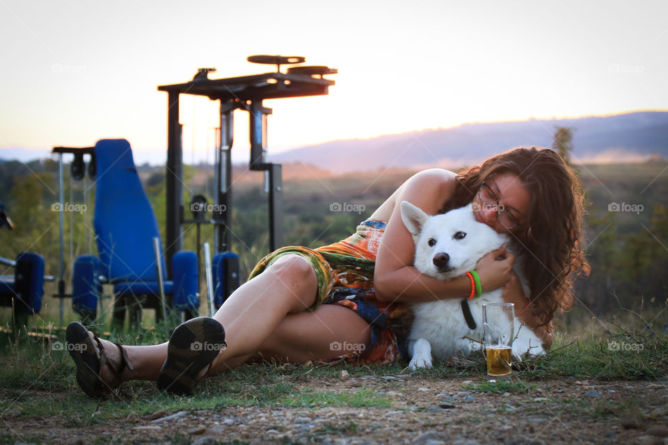 Young woman laying on the grass and hugging her white dog