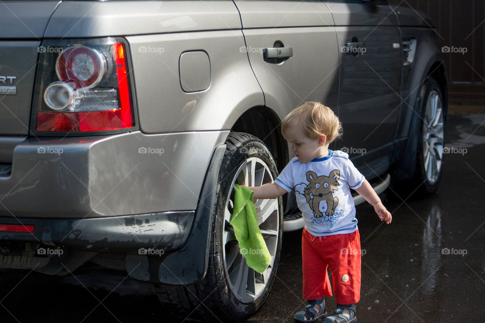 Cute little boy cleaning car wheel with cloth
