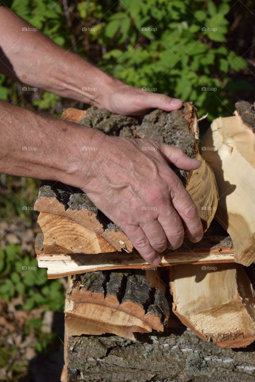 A Grandfather works hard stacking firewood to get ready for winter.