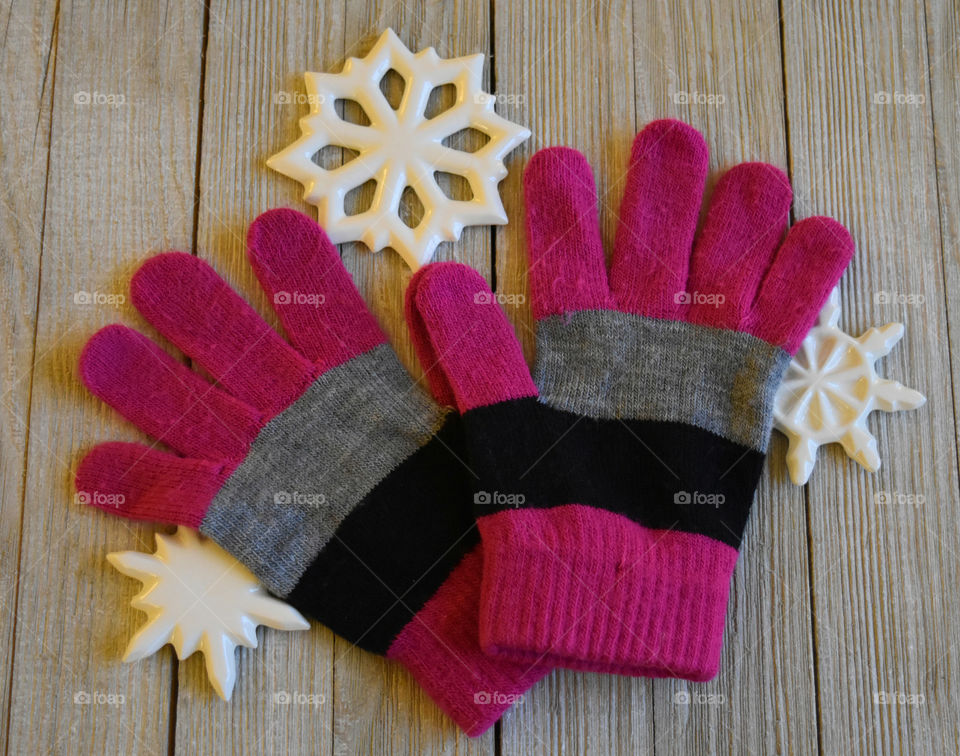 Colorful winter gloves with ceramic snowflakes on wood background