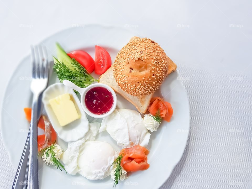 Delicious and healthy breakfast made by Benedict eggs, slice of res fish, vegetables, cheese cream, butter and cereals bread.