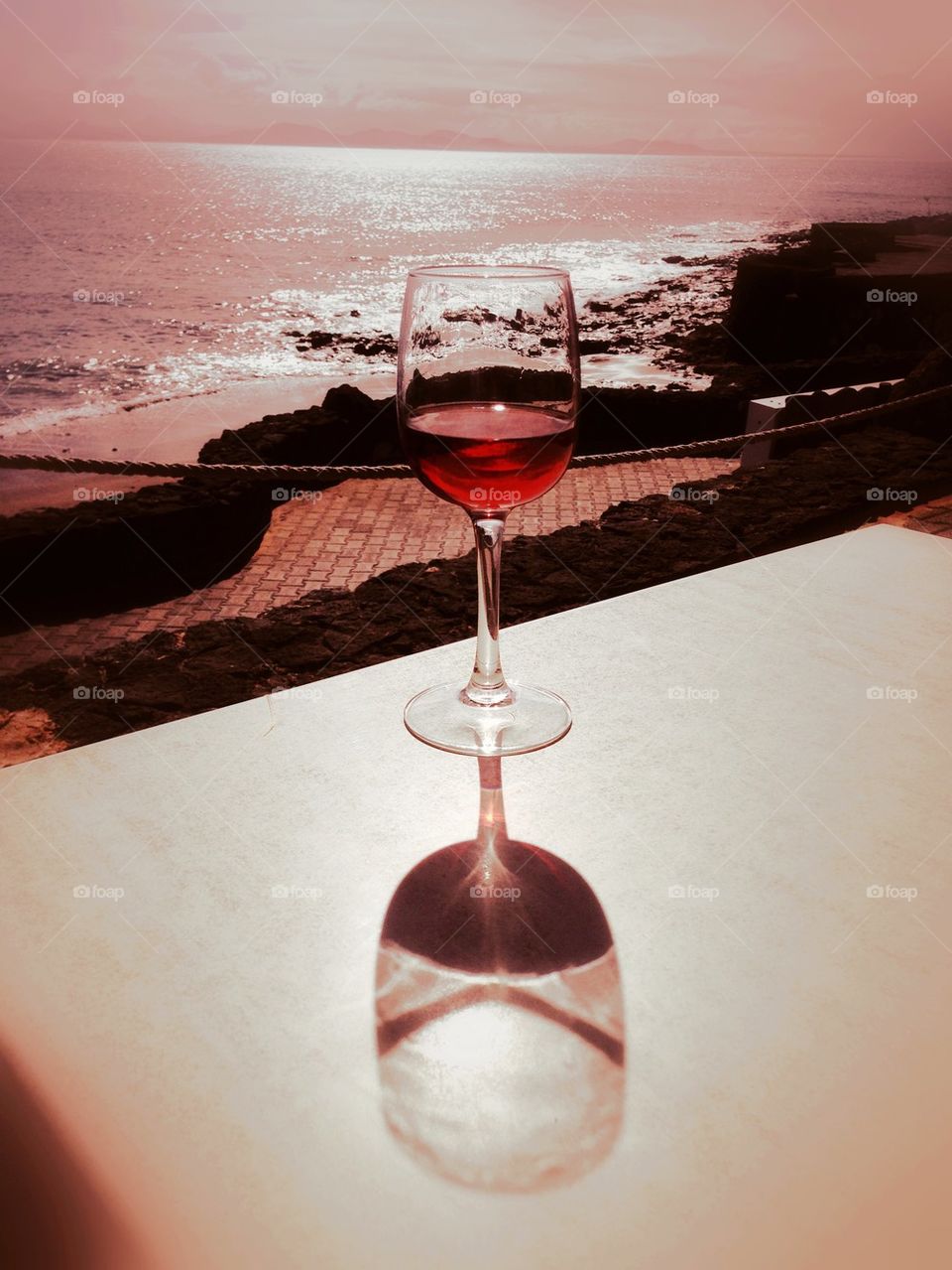 Reflection of red wine glass on table near the beach
