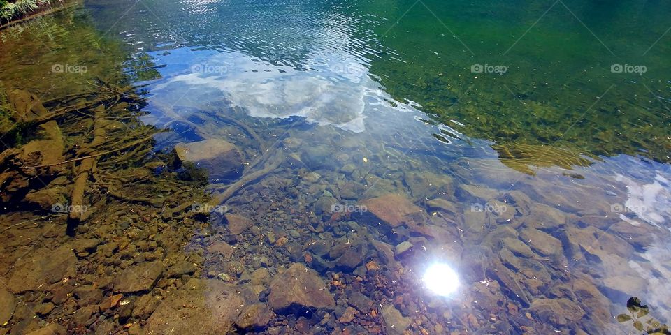 Clear blue water with rocks underneath and the reflection of the sky.