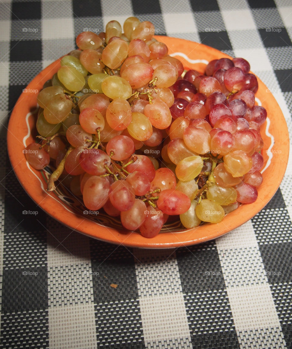 There are pink grapes on the table in a brown ceramic cup.