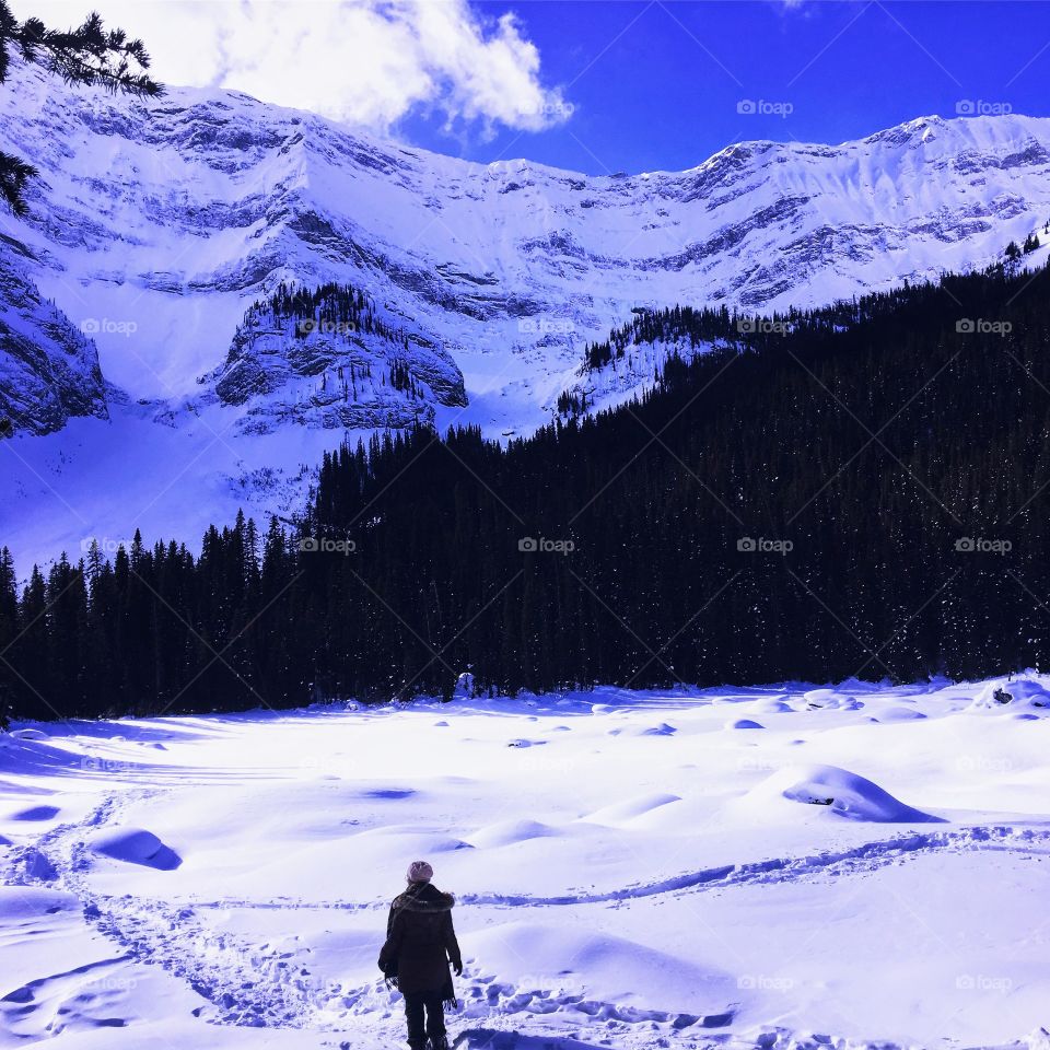 a girl snowshoeing in kananaskis through freshly powdered snow. taking in the view