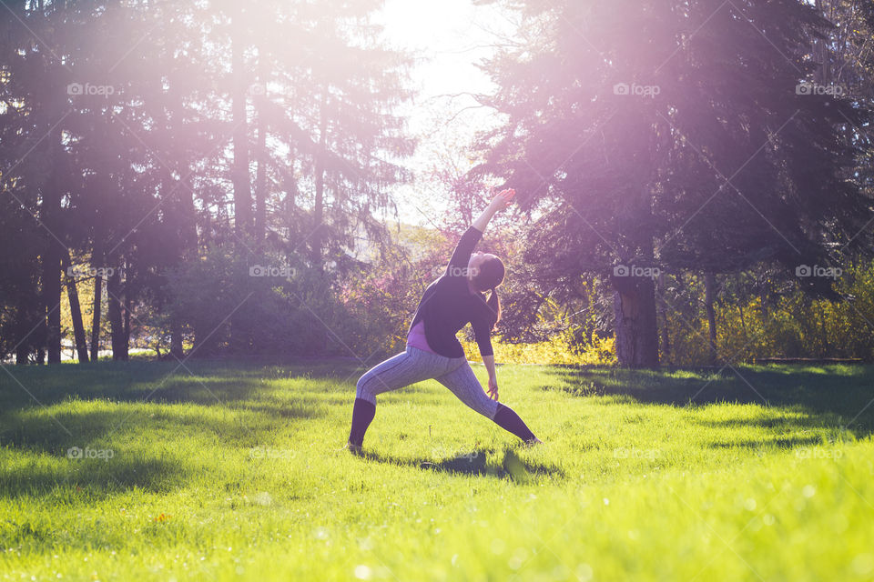 Beautiful natural light leaks into this photo of a yoga teacher during practice in an open field 