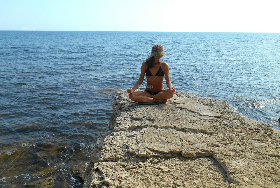 girl in yoga lotus on a sea stone shore summer time