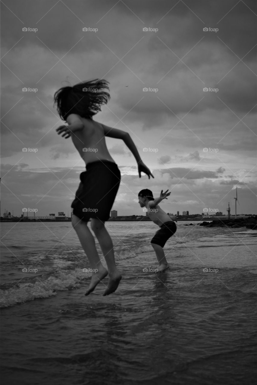 Two boys playing on the beach, jumping, action. having fun and loving life.