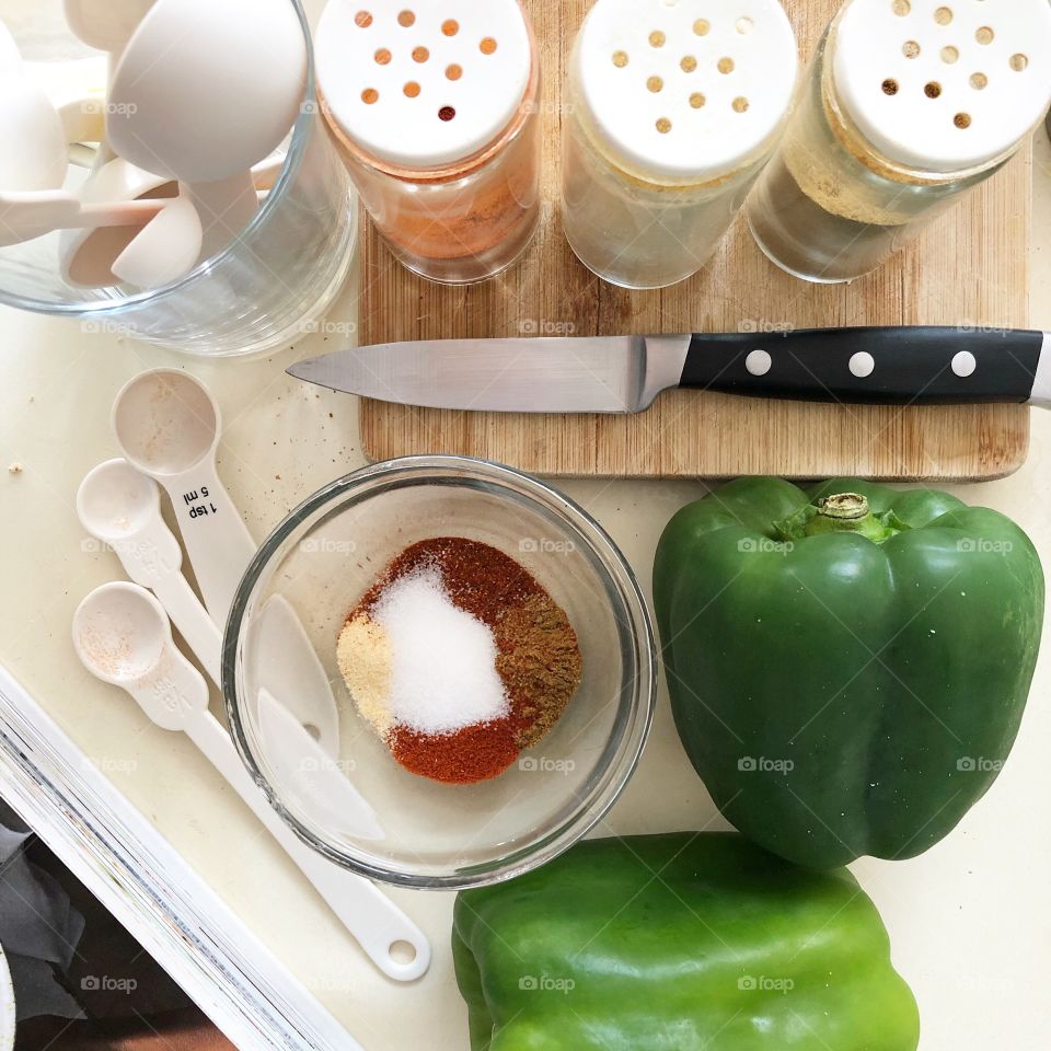 Meal preparation with spices, herbs, fresh vegetables, measuring utensils, knife, cutting board in a kitchen with a cookbook