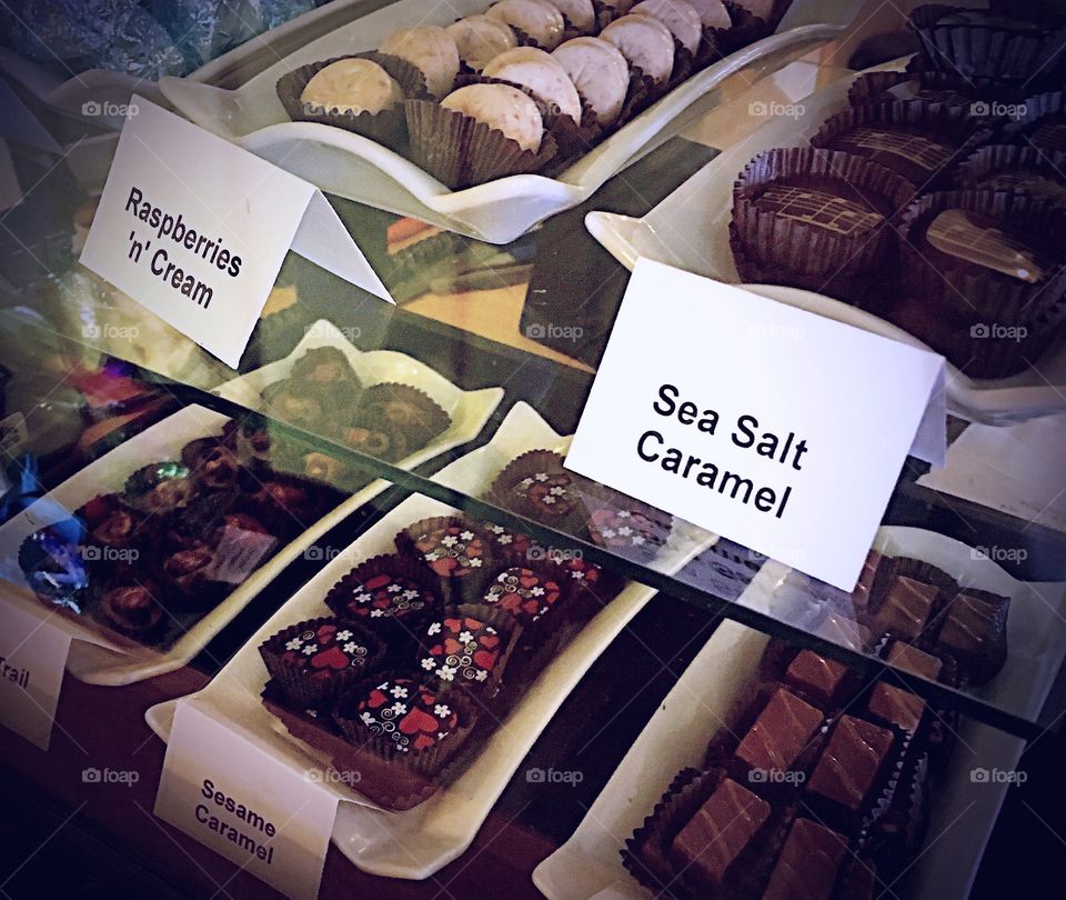 A variety of handmade artisanal chocolates for sale in a glass case. 