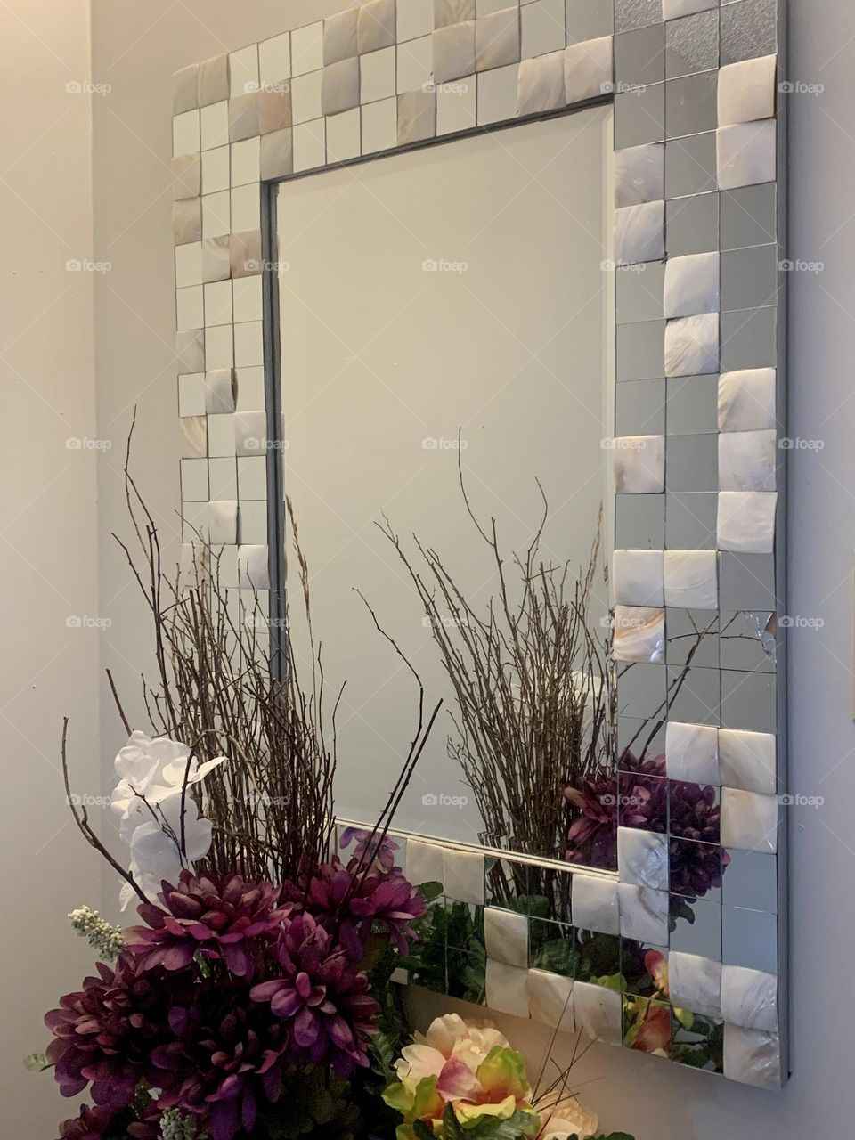 Rectangular mirror with tiny squared mirrored frame with flowers in the reflection 