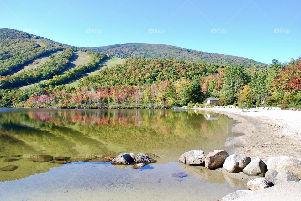 Autumn in New England, the calm water of the lake reflects the surrounding mountains covered in fall foliage