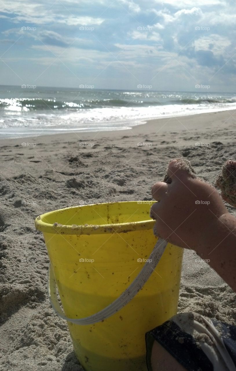 Toddler's hands on yellow bucket at beach
