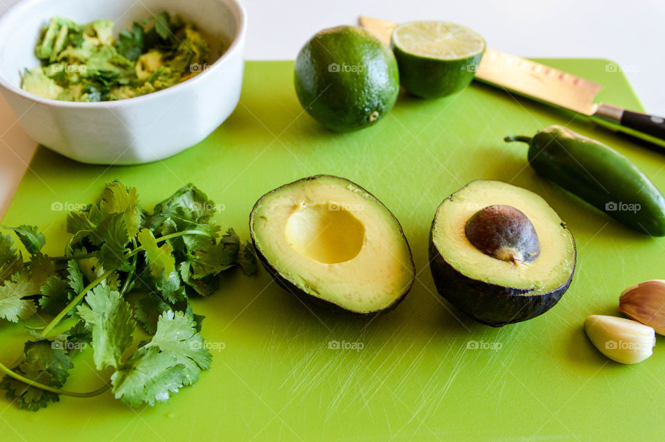 Green herb, fruit and vegetable ingredients for guacamole on a green cutting board