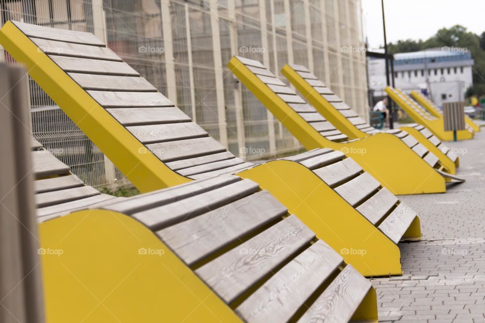 Modern, wooden bench with yellow edges in a metropolis. Corner of silence and calm.